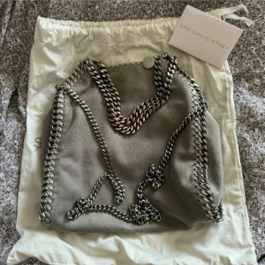 Grå axelväska från Stella McCartney - Ljusgrå Stella Mccartney Fallabella Mini! Kvitto och dustbag finns. Den är i superfint skick, dock har handtagen börjat släppa lite färg men det är inget som syns överdrivet mycket😊Nypris är ca 11 000kr och priset kan eventuellt sänkas lite vid snabbt köp! INGA BYTEN!!
