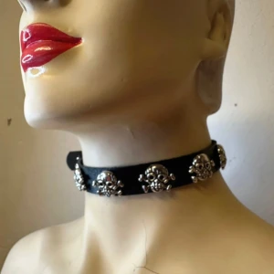 Ny svart choker med silvriga dödskallar – punkig & justerbar - Grym choker i svart faux leather med detaljerade dödskallar i metall – perfekt för alternativ stil med influenser från punk, goth eller rock. Justerbar längd (ca 30–42 cm) med spänne i nacken. Ca 2 cm bred. Oanvänd och i supersnyggt skick. Ingen prutning – men jag erbjuder gärna bundle-rabatt vid köp av flera plagg eller accessoarer! Rensar garderob & smyckesskrin – kika gärna på mina andra annonser också!  