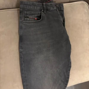Mörkgrå Diesel jeans tapered fit - Snygga mörkgrå jeans från Diesel med klassisk femficksdesign och diskreta slitningar. Modellen har tapered fit och normal midja, med Diesel-logga på bakfickan och läderpatch i midjan. Perfekta för en avslappnad men stilren look.
