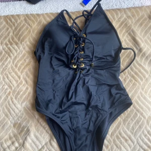 Svart baddräkt med snörning - Snygg svart baddräkt med snörning framtill och tunna axelband. Perfekt för stranden eller poolen, med en stilren och modern look. Aldrig använd.