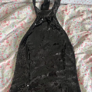 Svart paljett halterneck topp från ONLY - Säljer en svart halterneck topp från ONLY täckt med glittriga paljetter. Klänningen har halterneck och öppen rygg, vilket ger en snygg och festlig look. Perfekt för dig som vill sticka ut på festen!