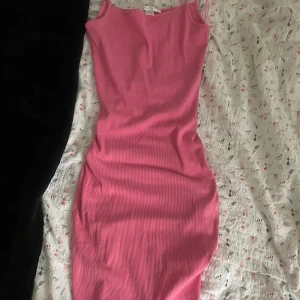 Rosa ribbad långklänning - Säljer en snygg rosa långklänning med ribbad struktur och smala axelband. Klänningen är figurnära och har en enkel, stilren design som passar perfekt till sommaren. Materialet är mjukt och stretchigt för en bekväm passform. Aldrig använd så i perfekt skick! 