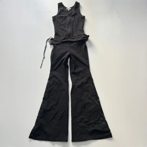 Jumpsuit - Svart sjukt snygg bootcut / vida ben jumpsuit från japanska märket Yokoo med snörning på sidorna och tillhörande bälte i midjan. Dragkedja på framsidan. Total längd (från axeln): 149 cm. Innerbenslängd: 79 cm