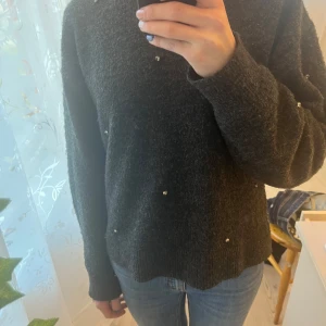Mörkgrå tröja med pärlor från H&M - Säljer en stilren mörkgrå tröja från H&M dekorerad med små pärlor. Tröjan har långa ärmar och en klassisk passform som passar perfekt för kyligare dagar. Perfekt för dig som vill ha något enkelt men med en twist.
