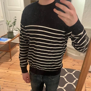 Marinblå och vit randig tröja från Uniqlo - Säljer en stilren svart tröja med vita ränder från Uniqlo. Tröjan har långa ärmar och en klassisk passform. Perfekt för en avslappnad look. Skick 10/10