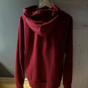 Röd dress - McKenzie - Säljer en fet mörk röd dress från McKenzie med dragkedja och justerbar luva. Perfekt för kyliga dagar med sin mjuka och bekväma passform. Den har långa ärmar och en liten logga på bröstet. Passar perfekt för en avslappnad stil.