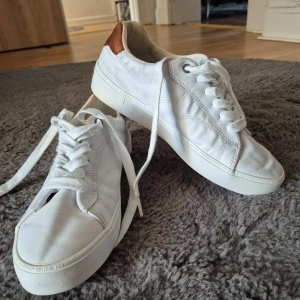 Vita sneakers med bruna detaljer - Snygga vita sneakers från Gant med bruna detaljer på hälen. Skorna har klassisk snörning och en stilren design som passar perfekt till vardags. Tillverkade i skinn för en lyxig känsla.