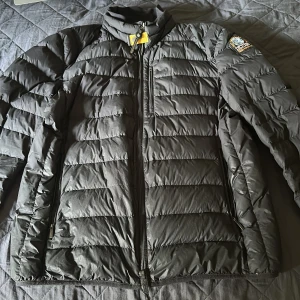 Svart pufferjacka från Parajumpers - Säljer en svart pufferjacka från Parajumpers. Jackan har en dragkedja framtill och är quiltad för extra värme. Perfekt för kyliga dagar med sin lätta och bekväma design. Märkesdetaljer på ärmen ger en snygg touch.