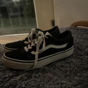 Svarta sneakers från Vans - Säljer ett par klassiska svarta Vans sneakers med vit sula och snörning. Skorna har den ikoniska vita sidostripen och är perfekta för en avslappnad stil. De är bekväma och passar till det mesta i garderoben.