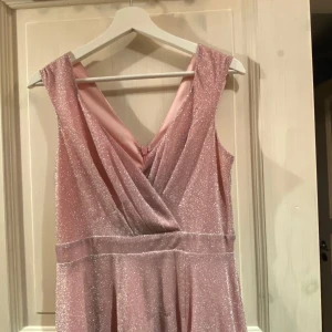 Rosa glittrig balklänning  - Säljer en fantastisk rosa lång ärmlös balklänning. Använd endast en gång! Rök- och djurfritt hem.. Storlek M. Använd endast en gång! .   Glittrig, snygg klänning från Goddiva. - Mjuk, stretchig kvalitet - V-ringad halsringning framtill och baktill - Fodrad - Slits framtill - Dold ryggdragkedja - Markerad midja Klänningen finns ny här:  https://www.bubbleroom.se/p/goddiva/klader/klanningar/maxiklanningar/glitter-wrap-maxi-dress-pink