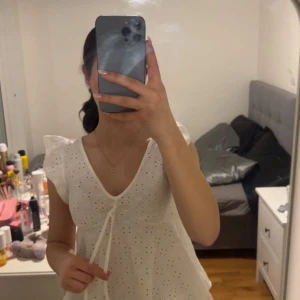 Vit blus med spetsdetaljer - Charmig vit blus med spetsdetaljer och knytning framtill. Blusen har korta ärmar med volang och en v-ringad hals. Perfekt för en somrig look.