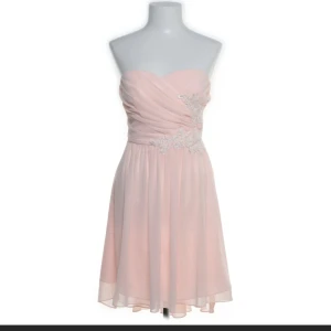 Ljusrosa axelbandslös klänning - Säljer en söt ljusrosa axelbandslös klänning med omlott-design och vackra spetsdetaljer vid midjan. Perfekt för sommarens fester eller en speciell kväll. Klänningen har en kort längd och ett luftigt fall.