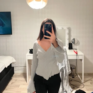 Grå ribbad tröja  - Säljer en stilren grå ribbad tröja. Tröjan har långa ärmar med en unik utsvängd design och en v-ringad hals. Perfekt för en trendig look. 