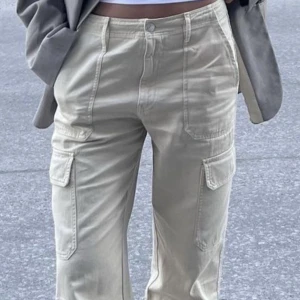Beige cargobyxor - Snygga beige cargobyxor med hög midja och raka ben. Byxorna har praktiska fickor på sidorna och en stilren design som passar perfekt till olika outfits. Perfekta för en avslappnad och trendig look.