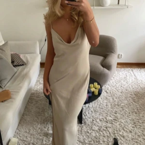 Beige långklänning från Meshki - Elegant beige långklänning från Meshki med en djup urringning och öppen rygg. Perfekt för en stilren och sofistikerad look. Klänningen har en smickrande passform och är tillverkad i ett mjukt material.