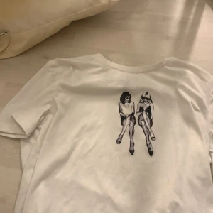 Vit t-shirt med tryck från Shein - Säljer en vit t-shirt från Shein med ett coolt tryck av två sittande figurer på framsidan. T-shirten har en normal passform och korta ärmar. Perfekt för en avslappnad stil!