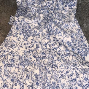 Vit och blå blommig klänning - Charmig vit klänning med blått blommönster. Passar superbra till en sommar avslutning!