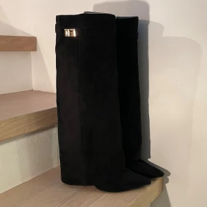 Svarta mockastövlar med klack - Snygga svarta stövlar i mocka med en elegant klack och dekorativt spänne upptill. De har en spetsig tå och är knähöga. Köpa på Vinted och använda 2 gånger. 