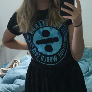 Svart t-shirt med blått tryck från Ed Sheeran - Säljer en svart t-shirt från Ed Sheerans Divide World Tour med ett stort blått tryck på framsidan och turnéstäder listade på baksidan. Perfekt för fans av Ed Sheeran! 🎶