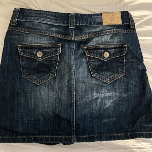 Vintage Jeanskjol  - Snygg jeanskjol från Cato med klassisk femficksdesign och dekorativa knappar på bakfickorna. Köpt på secondhand och är i storlek 40. Supersnygg till sommaren. 
