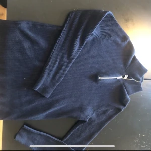 Mörkblå ribbad tröja med dragkedja - Snygg mörkblå tröja med ribbad struktur och dragkedja vid halsen. Perfekt för kyligare dagar med sin långa ärmar och stilrena design.