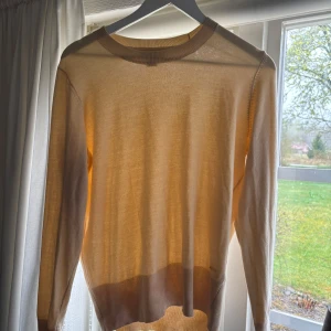 Beige stickad tröja från Holly & Whyte - Säljer en beige/gul stickad tröja från Holly & Whyte by Lindex. Den är i storlek L men jag som med storlek S har tyckt den sitter bra, lite lös men inte överdrivet. Tröjan har långa ärmar och fina guldfärgade knappar vid ärmsluten. 