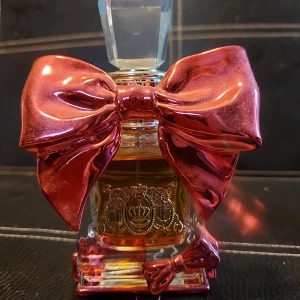 Viva La Juicy Bowdacious Eau de Parfum - Parfymflaska från Juicy Couture, Viva La Juicy Bowdacious. Flaskan är dekorerad med en stor, metallicrosa rosett och har en kristalliknande kork. Innehåller 50 ml eau de parfum med en lyxig och lekfull design.