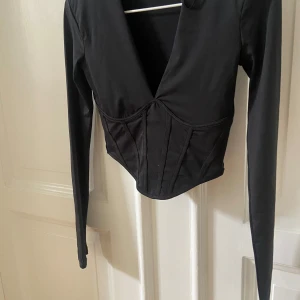 Svart korsettopp från Gina Tricot - Säljer en svart långärmad korsettopp från Gina Tricot. Toppen har en djup v-ringning och markerade sömmar som ger en snygg siluett. Den har typ ”puffiga axlar” eller något inlägg i axlarna så dem ser markerade ut. Säljer jättebilligt trots att det är i nyskick!!