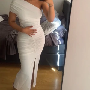 Vit one shoulder långklänning med slits - Säljer en elegant vit långklänning med one shoulder-design och draperade detaljer från Zara. Klänningen har en snygg slits framtill och figurnära passform som framhäver siluetten. Perfekt för speciella tillfällen!