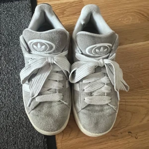 Adidas Campus  - Säljer ett par grå Adidas Campus sneakers i mjuk mocka med vita detaljer. Skorna köptes för 1100 och är i bra skick. Tveka inte på prisförslag!