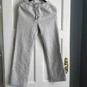 Grå mjukisbyxor från Gina Tricot - Grå mjukisbyxor från Gina Tricot med resår och dragsko i midjan. Byxorna har raka ben och är tillverkade i mjukt bomullsmaterial, perfekta för en avslappnad stil.