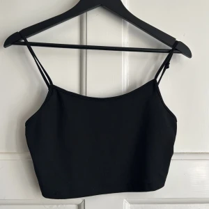 Svart croppad linnetopp med tunna axelband - Säljer en svart croppad linnetopp med dubbla tunna axelband. Toppen är tillverkad i stretchigt material och passar perfekt till sommaren. Enkel och stilren design som är lätt att matcha.