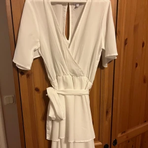 Vit omlottklänning från Bubbleroom - Säljer en stilren vit omlottklänning från Bubbleroom i storlek 32. Klänningen har kort ärm, v-ringning och knytband i midjan. Perfekt för sommarens tillfällen och har en feminin siluett med mjukt fallande tyg. Passar perfekt till student eller som en fin sommarklänning💞