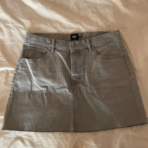 Grå jeanskjol från 157 - Säljer en stilren grå jeanskjol från 157 med klassisk femficksdesign och rå kant nertill. Kjolen har bälteshällor och stängs med knappar framtill. Jag är inte helst säker på storleken då den lappen inte sitter kvar på kjolen men kjolen passar både L och M. Kjolen är använd ett fåtal gånger. 