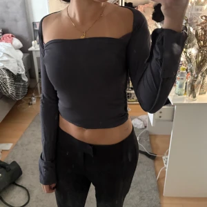 Svart offshoulder topp - Trendig svart offshoulder topp med långa ärmar och tight passform. Perfekt för dig som vill ha en stilren och enkel look med en twist. Toppen är croppad och har en rak skärning över bröstet.