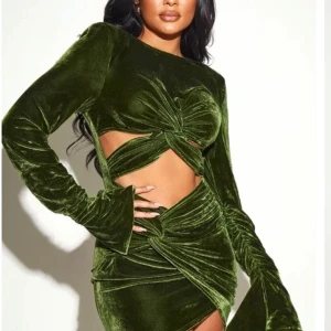 Grön sammetsklänning från PrettyLittleThing - Säljer en grön sammetsklänning från PrettyLittleThing med långa ärmar, cut-out detaljer och twistad omlott-effekt framtill. Klänningen har figurnära passform och dragkedja i ryggen. Använd endast gång och är i princip helt ny. Obs etikett med storlek har gått av på ena sidan. 