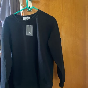 Svart sweatshirt från Stone Island - Säljer en svart sweatshirt från Stone Island med klassisk rund hals och lång ärm. Tröjan har den ikoniska Stone Island-loggan på ärmen och är tillverkad i mjuk bomull. Perfekt för en stilren och avslappnad look.
