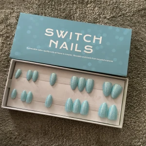 Blå glittriga lösnaglar från Switch Nails - Säljer ett set med återanvändbara lösnaglar i färgen Blueberry Milk Pixie från Switch Nails. Naglarna har en mandelform och är korta, med en ljusblå bas och glittereffekt. Perfekt för dig som vill ha snygga naglar snabbt! Kommer utan tillbehör.