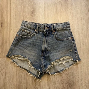 Blå jeansshorts - Säljer ett par blå jeansshorts från ZARA med hög midja och lite fransade kanter. Klassisk femficksmodell med slitna detaljer och knappgylf. Perfekta för varma dagar. Skriv om du har frågor o läs gärna min bio innan du köper🫶🏻🫶🏻