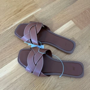 Bruna sandaler med flätad rem från H&M - Bruna sandaler från H&M med breda, flätade remmar och fyrkantig tå. Skorna har platt sula. Säljer för jag råkade beställa 2 likadana.