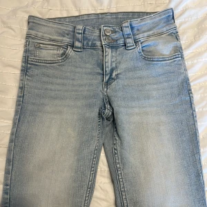 Ljusblå bootcut jeans från H&M - Säljer ett par ljusblå bootcut jeans från H&M med låg midja och justerbar midja. Jeansen har klassiska fickor fram och bak med knappdetaljer på bakfickorna. 