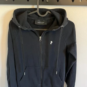 Svart hoodie från Peak Performance - Svart peak performance hoodie med dragkedja och dragsko. Använd ett fåtal gånger och är i storlek xs. Är i väldigt bra skick. Köpte den för 1200kr.