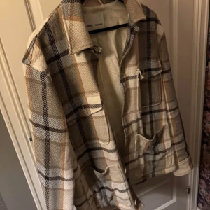 Rutig overshirt från Samsøe Samsøe - Säljer en snygg rutig overshirt från Samsøe Samsøe i beige, brunt och svart. Jackan har klassisk krage, stora fickor framtill och knäppning. Perfekt lager-på-lager-plagg med lång ärm och mjukt material.