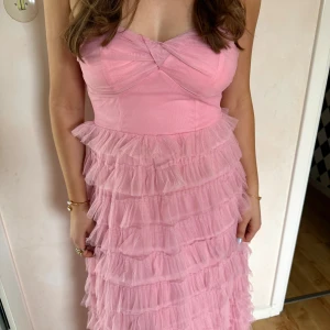 Rosa långklänning med volanger från Hello Molly - Supersöt och drömmig klänning från Hello Molly som är helt ny och oanvänd. Den perfekta balklänningen eller för andra speciella sommar tillfällen. Super skön och fin axelbandslös klänning, med ett luftigt och vackert tyg. 