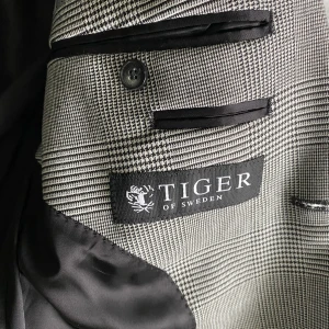 Grå rutig kavaj från Tiger of Sweden storlek 48 - Snygg grå kavaj med rutigt mönster från Tiger of Sweden. Kavajen har två knappar framtill, klassisk krage och svarta innerfickor. Perfekt för en stilren look.