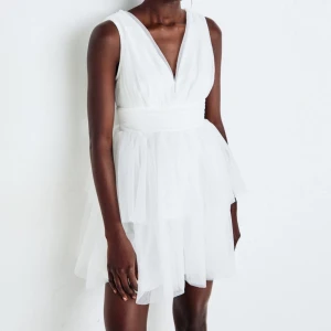 Studentklännign - Supersöt vit kortklänning med v- ringning och markerad midja. Klänningen har flera lager tyll som ger en fluffig och romantisk känsla. Perfekt för studenten. Hade den själv på studenten och har ej använts mer efter det. 