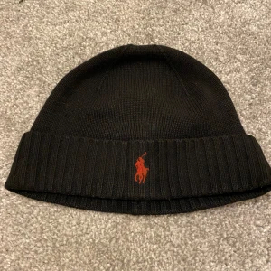  Ralph Lauren mössa - Svart stickad mössa från Polo Ralph Lauren med röd broderad logga framtill. Tillverkad i mjuk och tvättbar merinoull. Klassisk ribbad kant för extra komfort och stil. Pris ej hugget i sten kom med förslag 😃