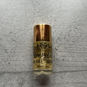NYX Honey Dew Me Up Primer - NYX Honey Dew Me Up Primer med guldglittrande partiklar och genomskinlig gelkonsistens. Kommer i en liten glasflaska med guldfärgat lock. Perfekt för att ge huden lyster innan smink. Har aldrig använts eller öppnats.