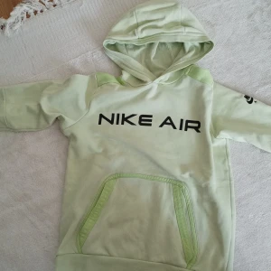 Nyongrön hoodie från Nike Air - Säljer en ljusgrön hoodie från Nike Air med svart logga på bröstet och ärmen. Tröjan har huva och en stor magficka framtill. Perfekt för dig som gillar sportig stil och vill ha något bekvämt och snyggt. OBS! Har en knappt synlig röd fläck på baksidan.