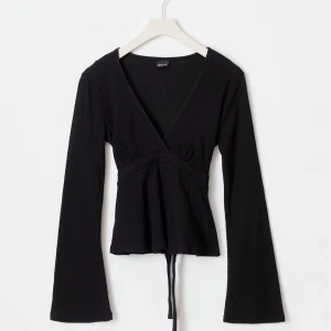 Tie top - Svart långärmad omlottopp med v-ringning och knyt i midjan. Toppens material är lätt och har en diskret struktur. Perfekt för att skapa en stilren och trendig look.